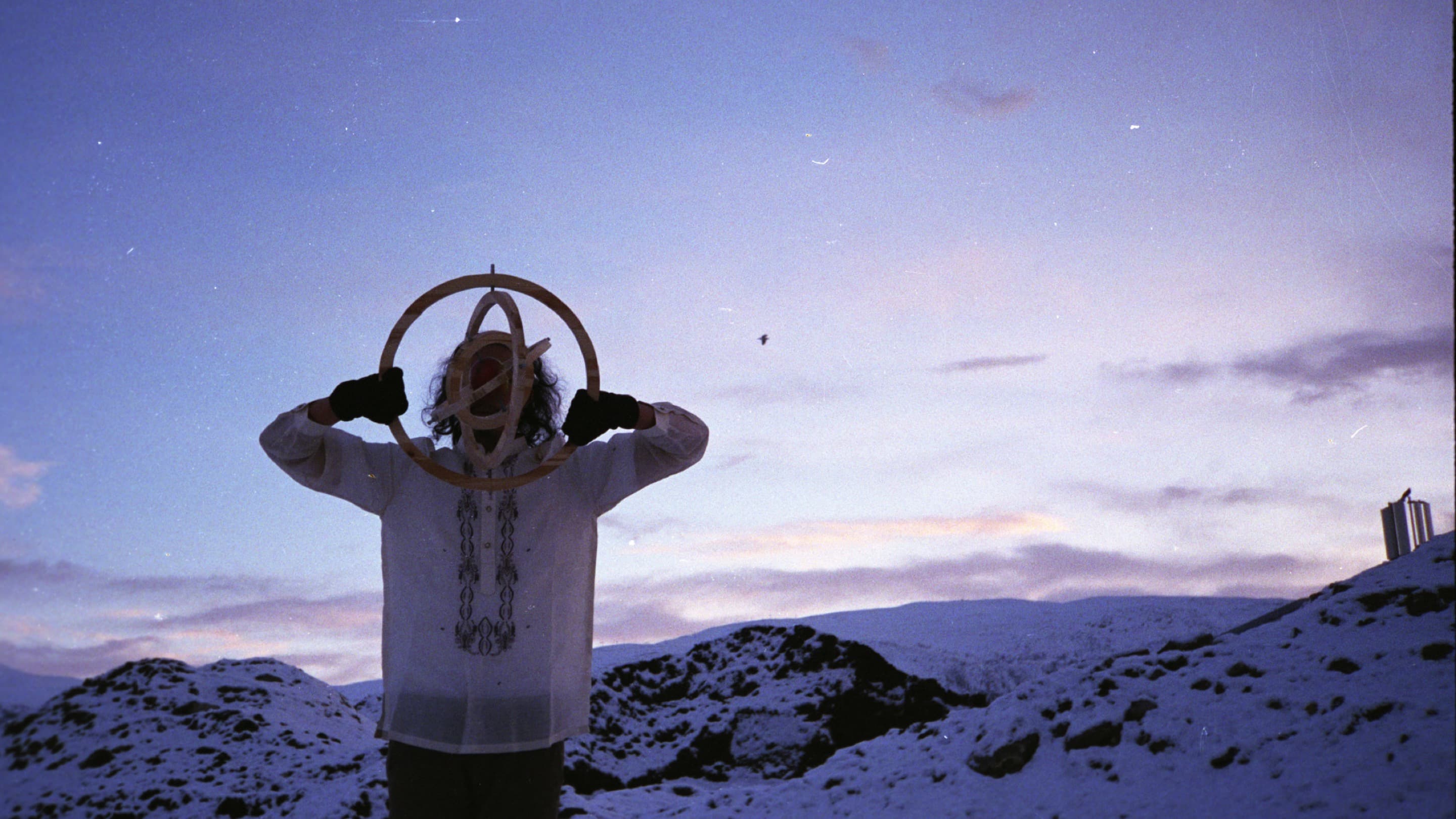 A man stands holding mobile artwork against a background of snow-covered mountains at dawn. 