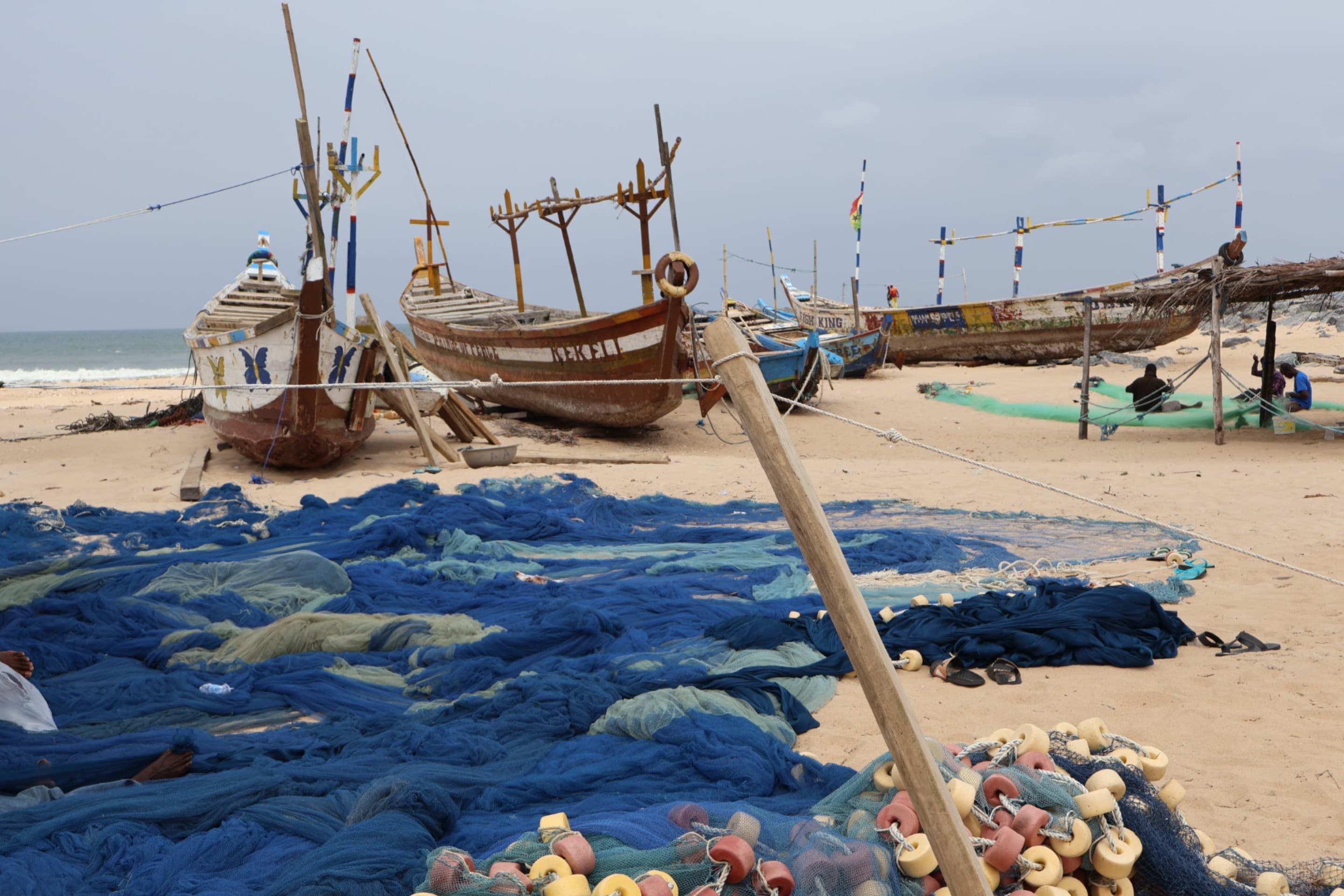 A line of wooden ships with fishing nets in the foreground on a beach in Keta, Ghana.