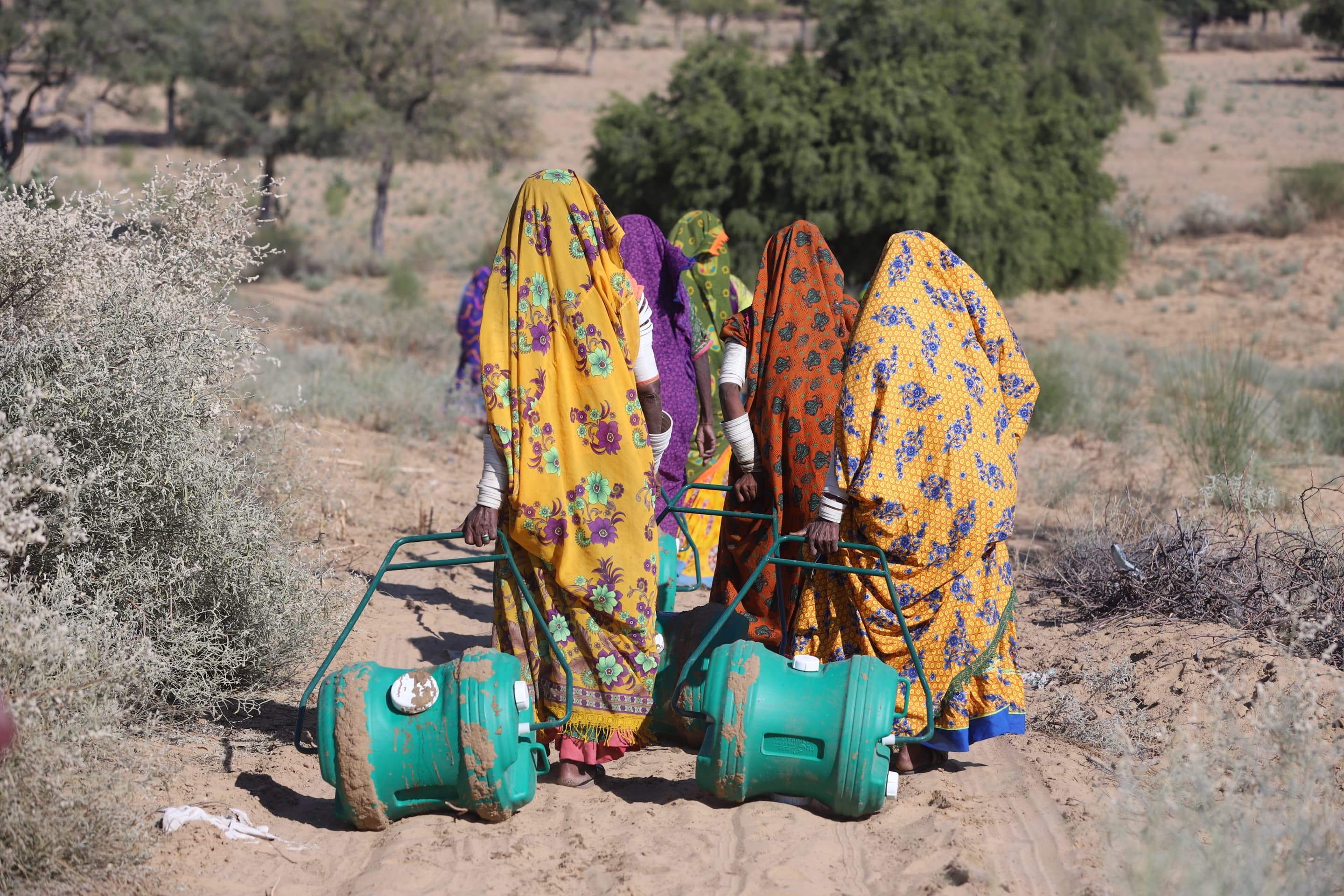 A group of women in colourful, traditional Pakistani dress trundle along H2O's turquoise-colored water carriers in rural Pakistan.