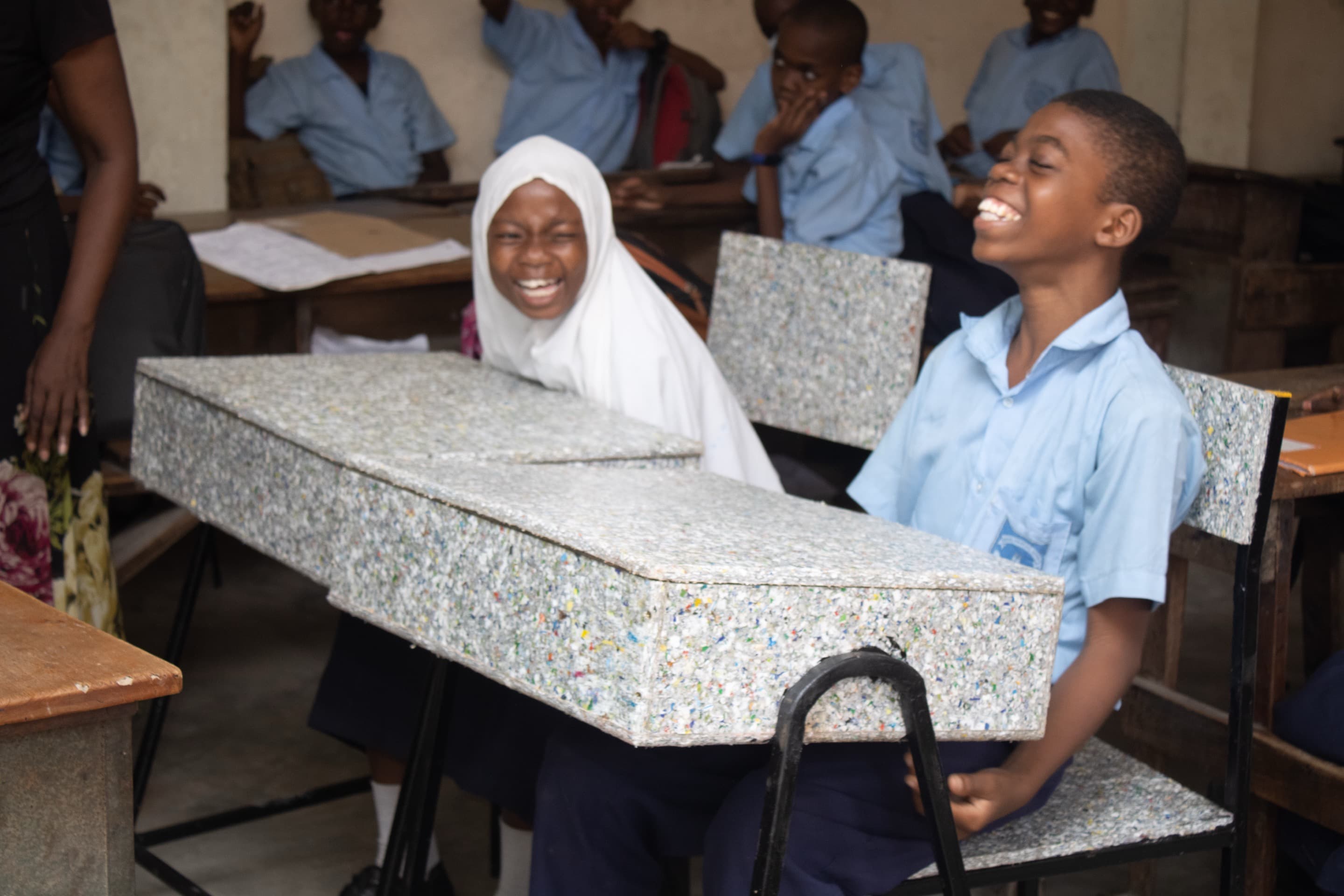 School children laugh while sat at Twende Green Ecocycle's recycled plastic desks.