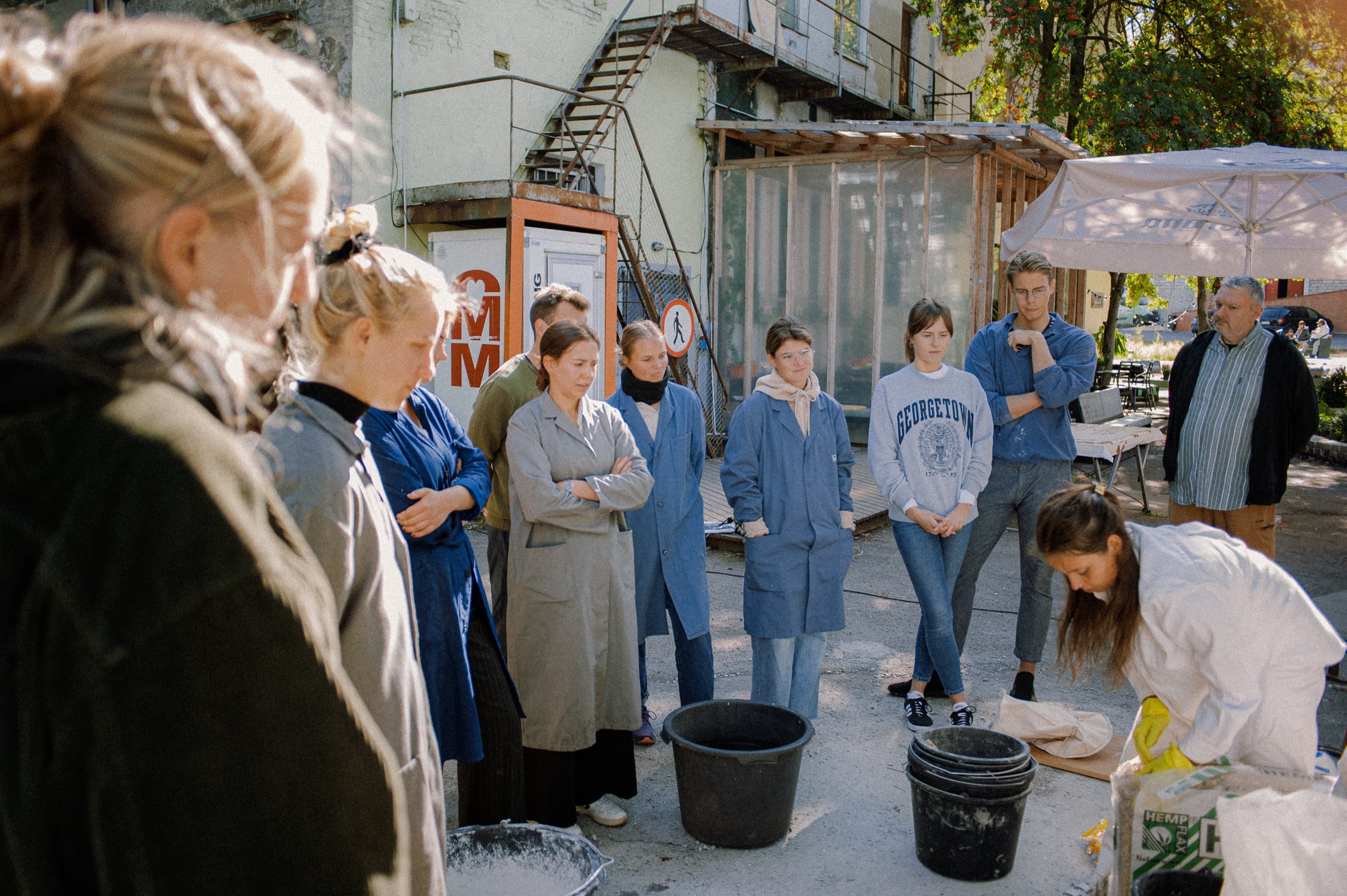 Participants stand around Hannah Segerkrantz as she leads a hempcrete-making workshop.