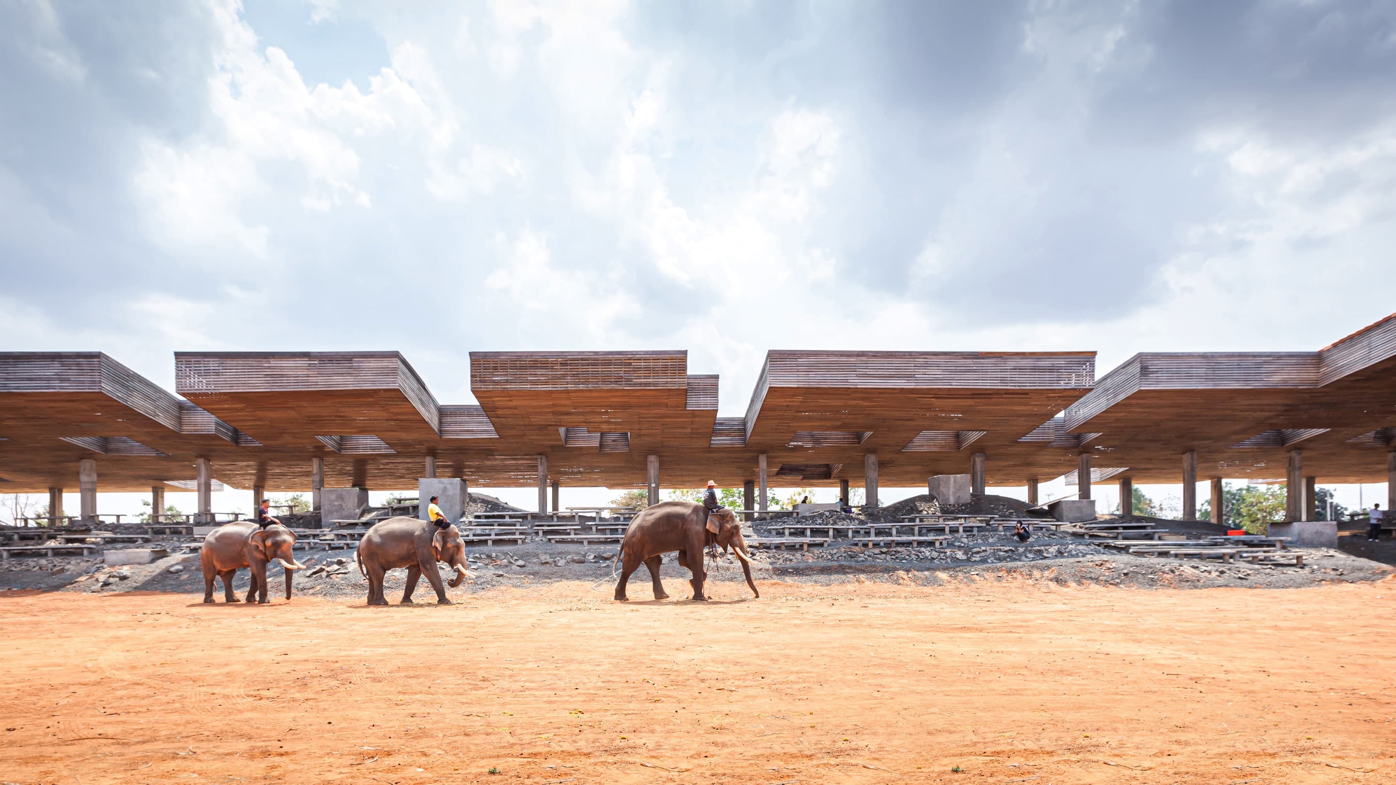 Three people ride elephants across the Elephant Center by Boonserm Premthada.