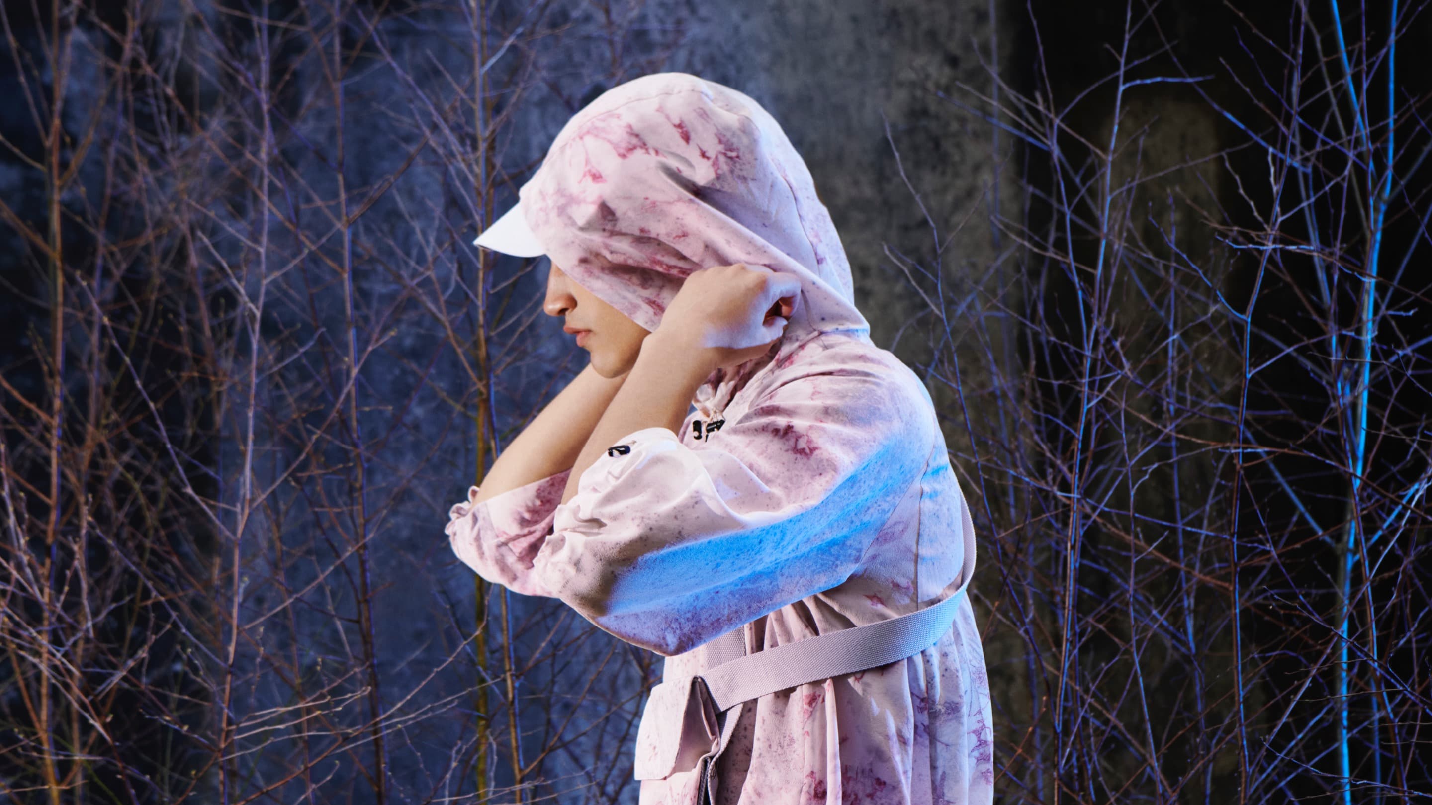 A person wearing a pink hooded jacket with a hood against a background of trees.