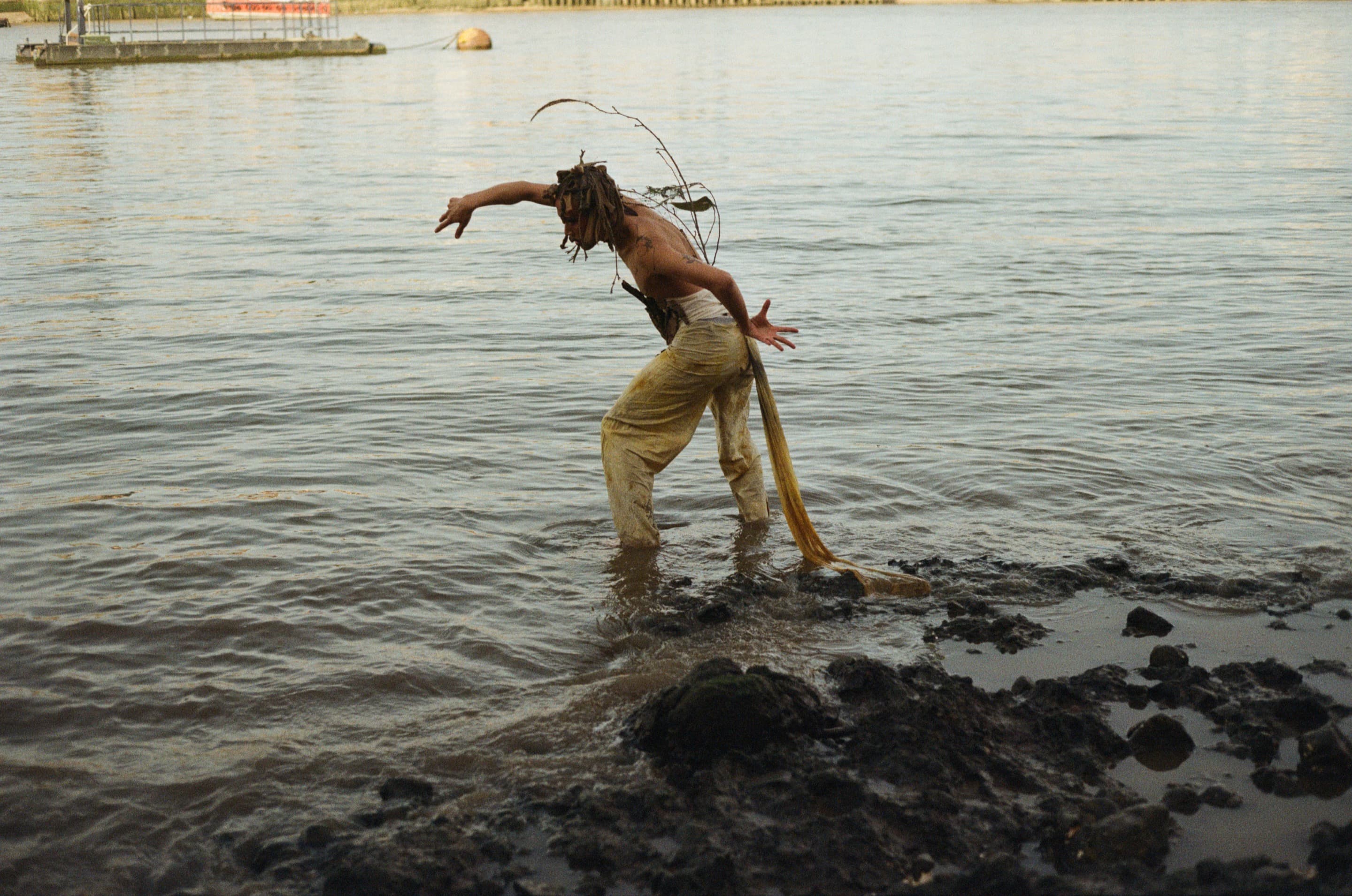Owen Chiou wades into a brown river in a still from his multi-media project We never fall apart because we never fall together.