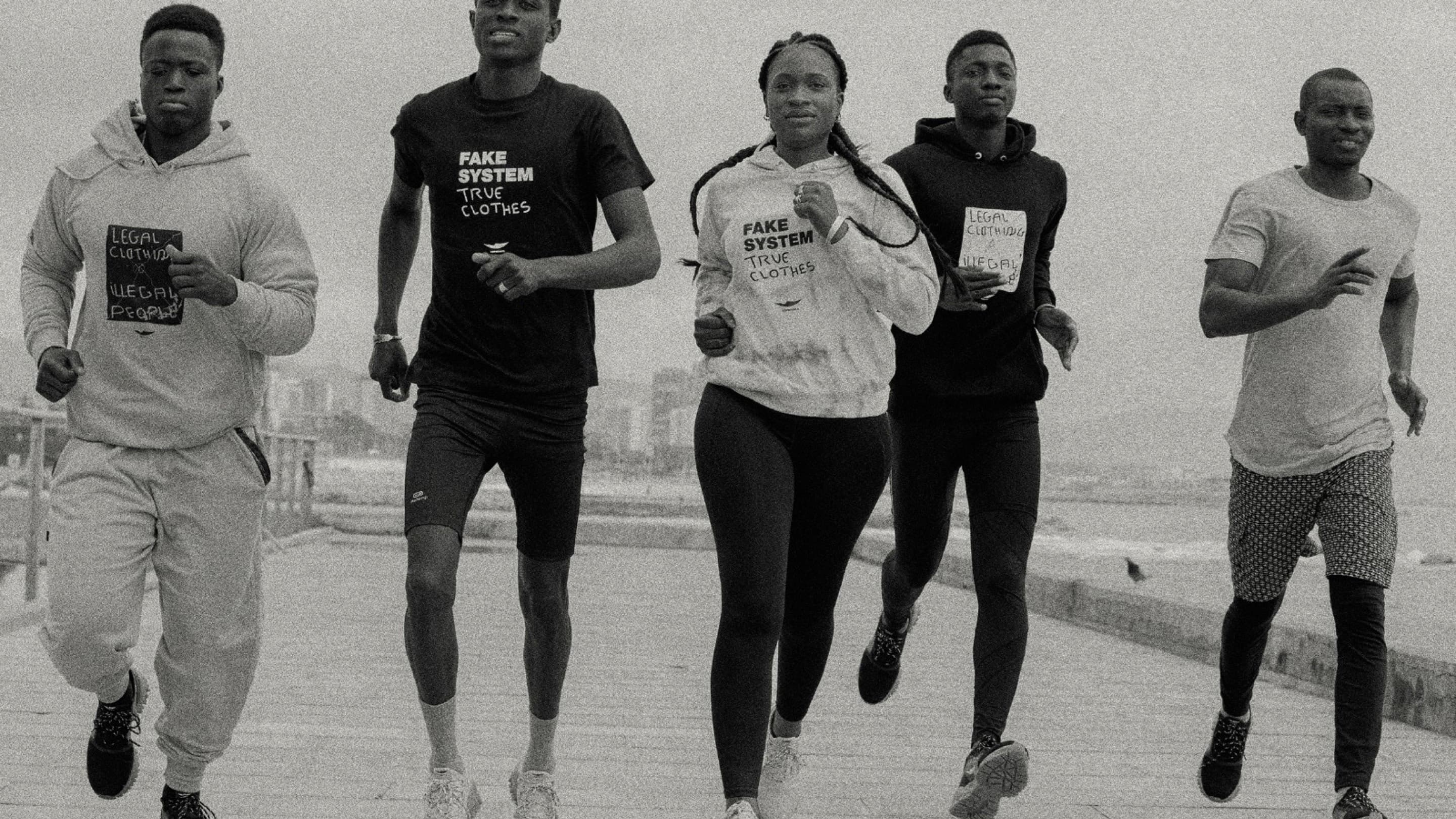A group of people running in sportswear. The text on their hoodies reads: "Fake System, True Clothes".